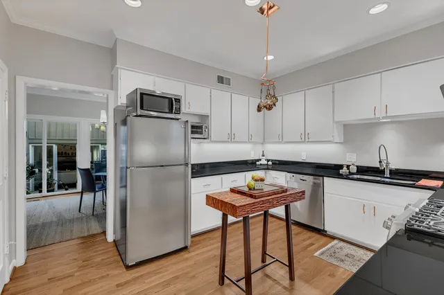 a kitchen with stainless steel appliances granite countertop a refrigerator a sink a stove a dining table and chairs with wooden floor