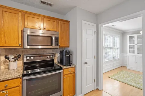 a view of an empty room with chandelier fan and kitchen view