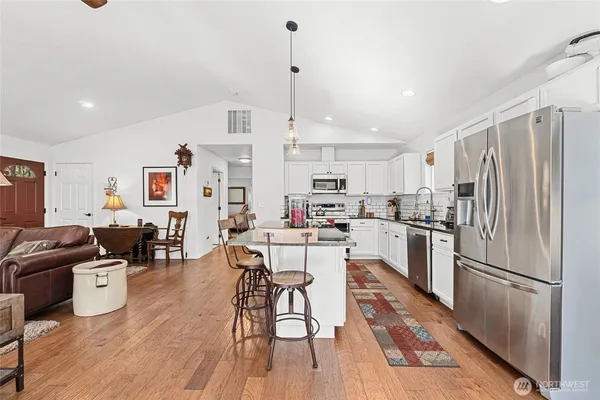 a kitchen with stainless steel appliances a refrigerator a stove top oven a dining table and chairs with wooden floor