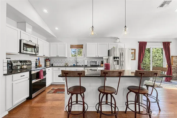 a kitchen with stainless steel appliances kitchen island granite countertop a stove a sink a refrigerator and white cabinets with wooden floor