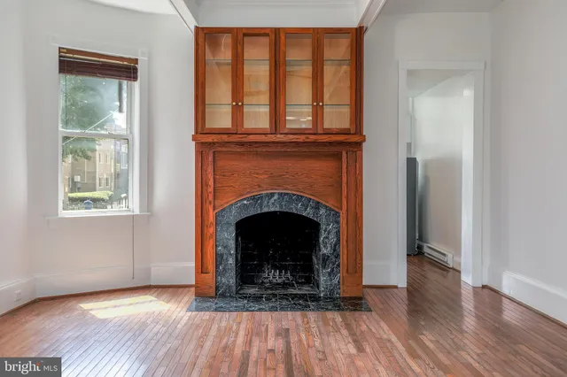 a view of an empty room with wooden floor fireplace and a window