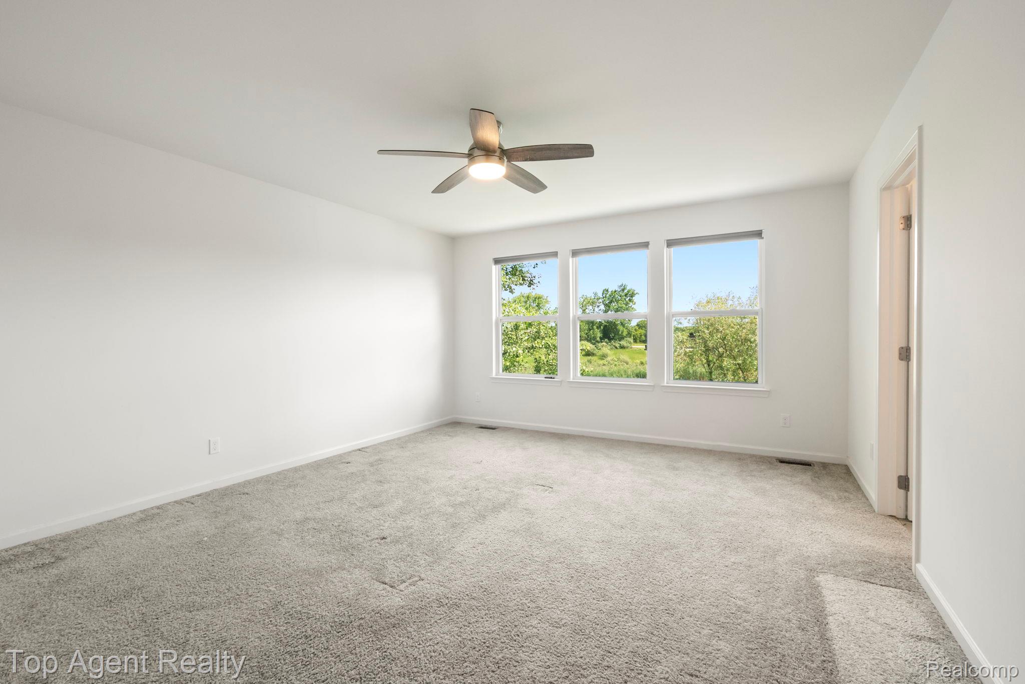 63770 Dequindre Road Washington, MI 48095 - Photo 41 of 61 Spacious room featuring light gray carpeting, a contemporary ceiling fan with lighting, and a wall of three large windows providing abundant natural light and green scenery