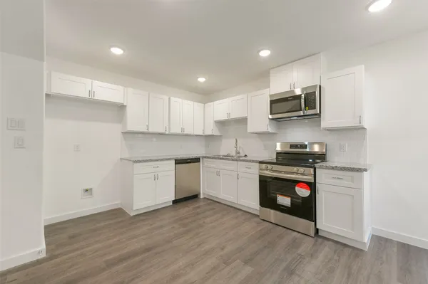 a kitchen with stainless steel appliances white cabinets a sink a stove a microwave and wooden floors