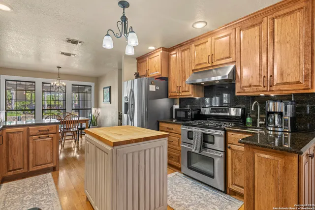 a kitchen with stainless steel appliances granite countertop a stove top oven a sink dishwasher and a refrigerator with wooden cabinets