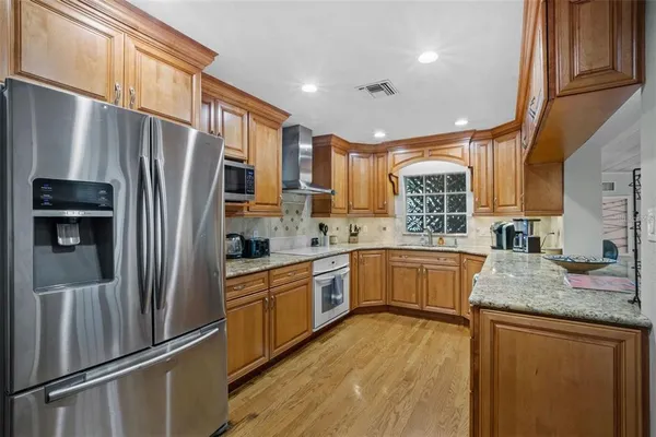 a kitchen with stainless steel appliances granite countertop a refrigerator a sink dishwasher a stove with white cabinets and wooden floor