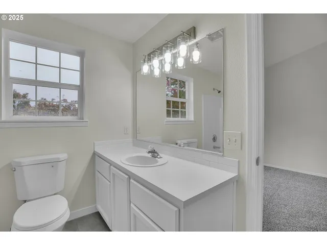 a bathroom with a sink a toilet a mirror and a window