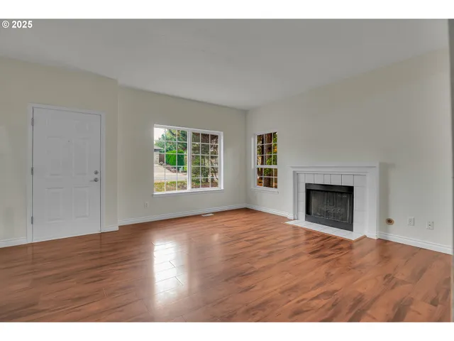 a view of an empty room with wooden floor fireplace and a window