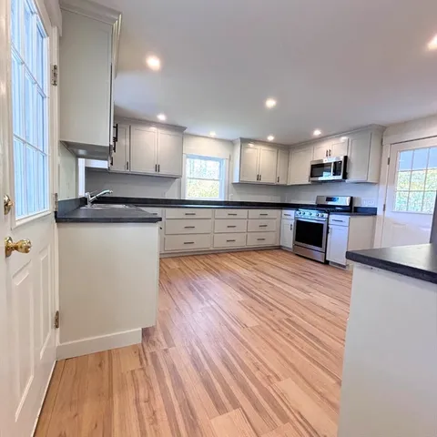 a large kitchen with stainless steel appliances granite countertop a stove a sink dishwasher and a refrigerator with wooden floor