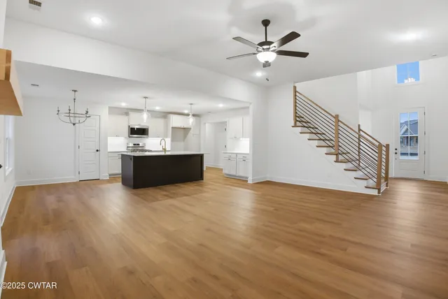 a view of an empty room with wooden floor and a ceiling fan