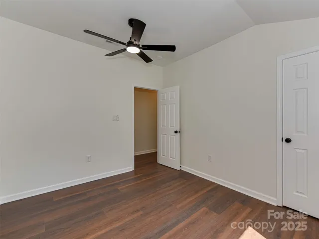 a view of an empty room with wooden floor and a ceiling fan