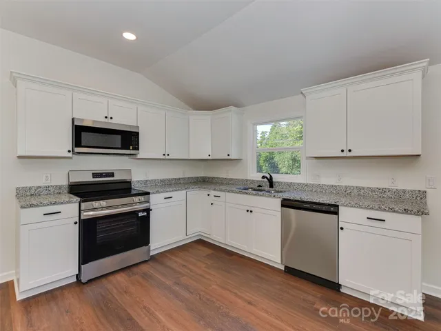 a kitchen with granite countertop white cabinets stainless steel appliances and a wooden floor