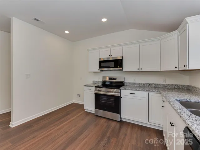a kitchen with granite countertop white cabinets a sink a window and wooden floor