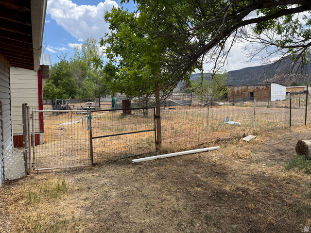 210 South State Street Moroni, UT 84646 - Photo 21 of 23 Fenced yard area featuring a metal gate and mature trees, with a distant building and mountainous backdrop