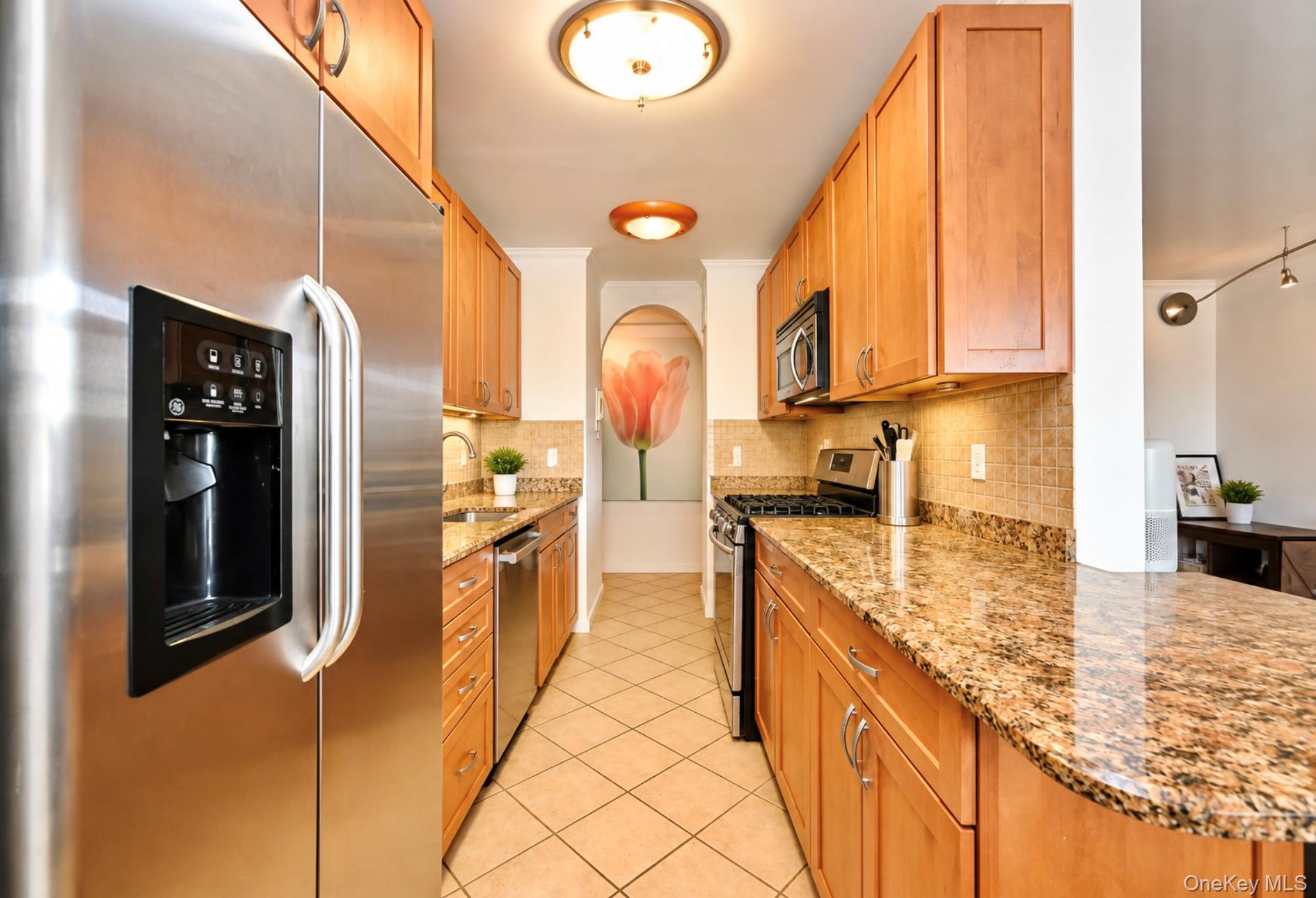 102-30 66th Road, Unit 17E Queens, NY 11375 - Photo 5 of 21 Galley kitchen featuring stainless steel appliances, wood cabinetry, granite countertops, and tile flooring