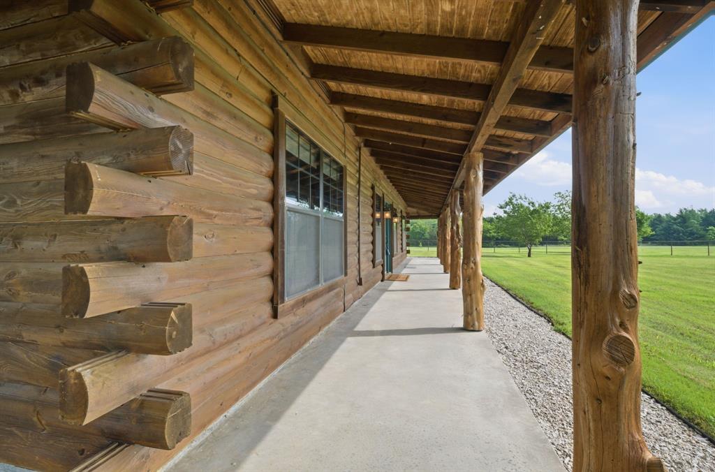 465 Emberson Ranch Road Pilot Point, TX 76258 - Photo 21 of 37 Log cabin exterior with exposed log construction, a covered porch with natural wood posts, wood-plank ceiling, and a concrete walkway