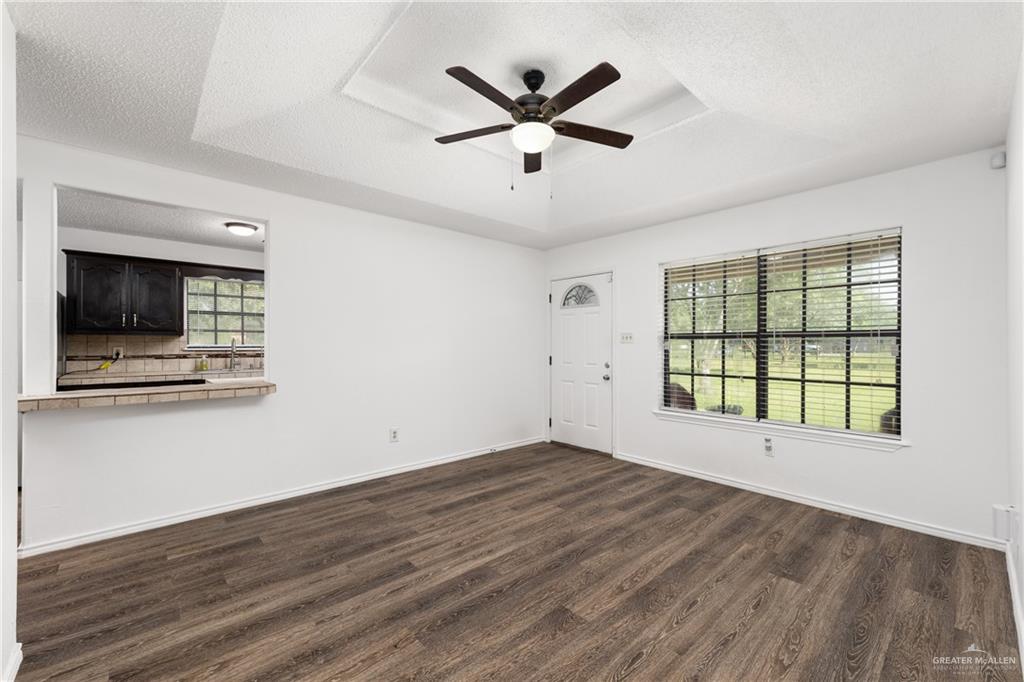 20538 Rio Rancho Road Harlingen, TX 78552 - Photo 2 of 19 Unfurnished living room with a tray ceiling, dark wood-style flooring, ceiling fan, and a textured ceiling