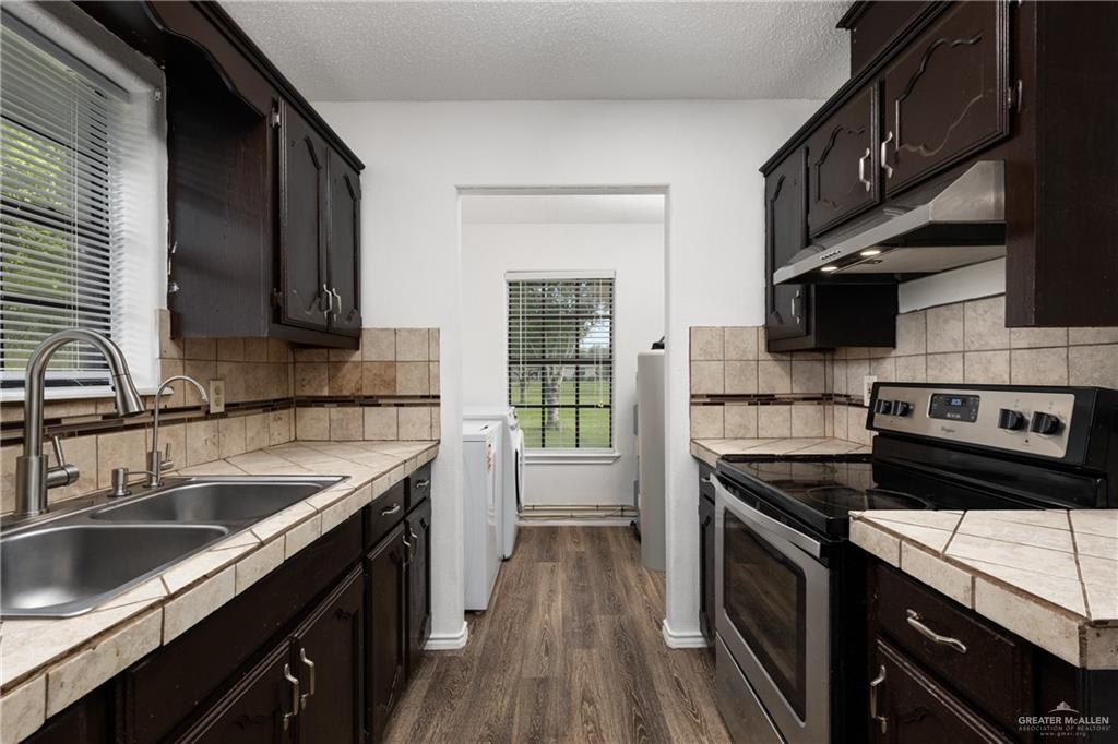 20538 Rio Rancho Road Harlingen, TX 78552 - Photo 3 of 19 Kitchen with electric stove, washing machine and clothes dryer, under cabinet range hood, tile countertops, and dark wood-style floors