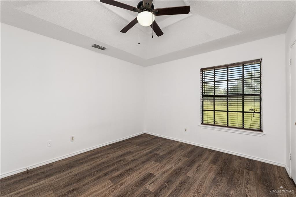 20538 Rio Rancho Road Harlingen, TX 78552 - Photo 5 of 19 Empty room with dark wood-type flooring, ceiling fan, and a tray ceiling