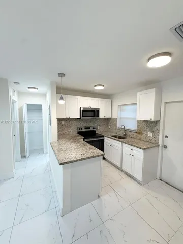 a large kitchen with granite countertop a sink and white cabinets