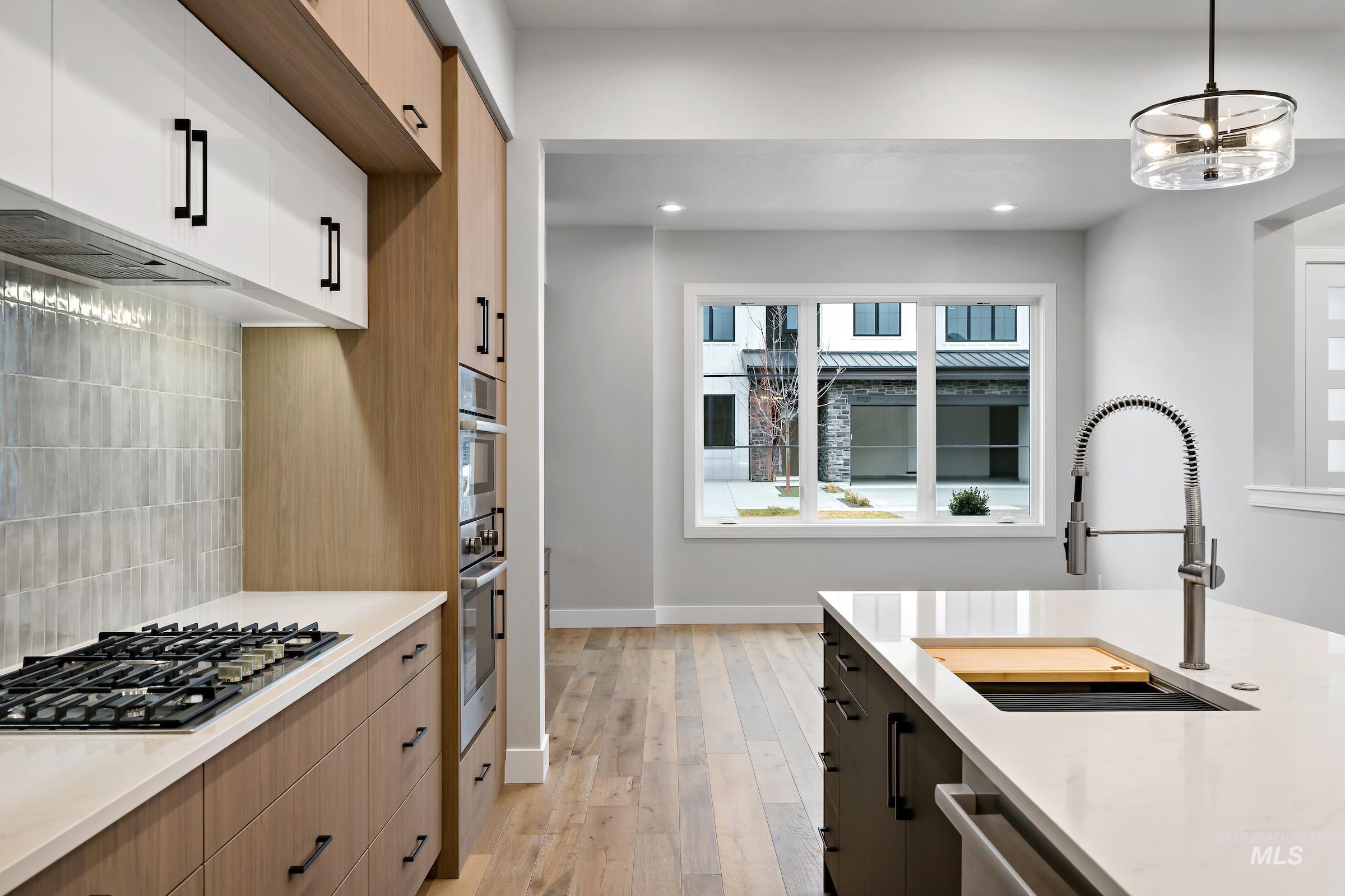 11725 North Rabbitbrush Way Boise, ID 83714 - Photo 18 of 36 Kitchen featuring pendant lighting, decorative backsplash, light stone counters, stainless steel appliances, and light wood-type flooring