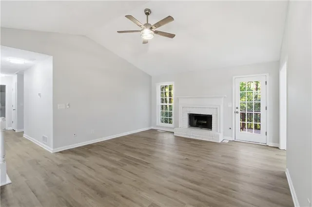 an empty room with wooden floor a ceiling fan a fireplace and windows