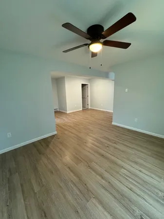 an empty room with wooden floor ceiling fan and windows