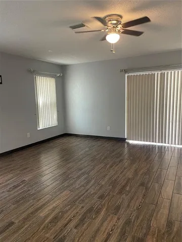 an empty room with wooden floor chandelier fan and windows
