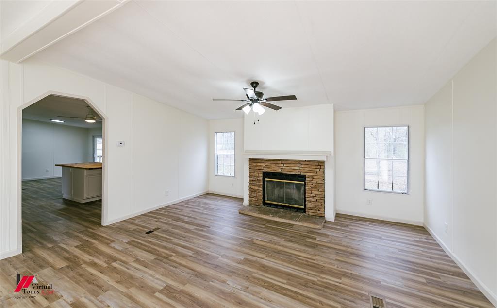 4947 Quiet Acres Road Shreveport, LA 71107 - Photo 7 of 39 Unfurnished living room featuring arched walkways, a ceiling fan, light wood-style flooring, and a fireplace