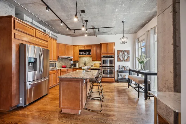 a kitchen with stainless steel appliances granite countertop a refrigerator a oven a stove and a dining table with wooden floors