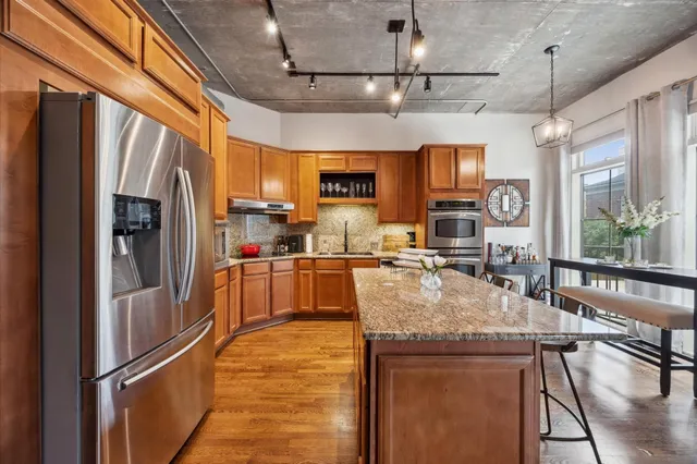 a large kitchen with stainless steel appliances granite countertop a refrigerator a sink dishwasher a stove and a refrigerator with wooden floor