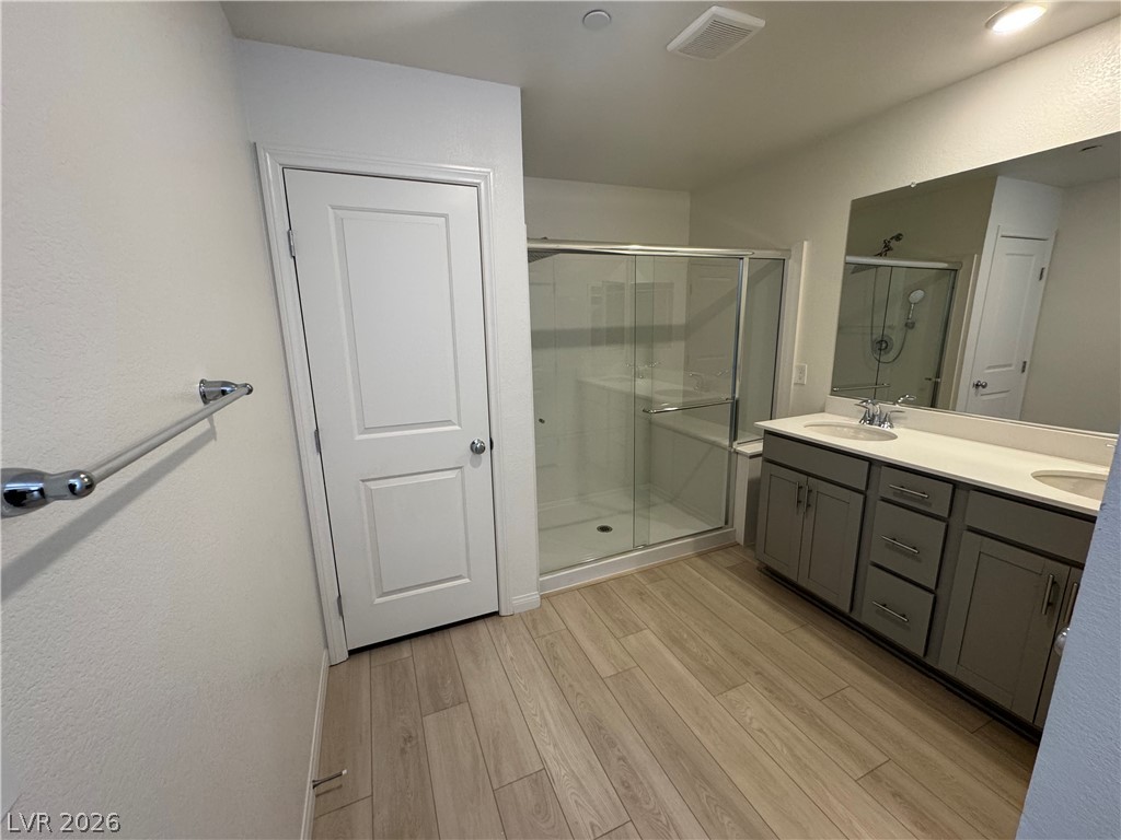 2821 Alcobaca Street Henderson, NV 89044 - Photo 23 of 24 Dual vanities complement a contemporary bathroom with a glass-enclosed shower and wood-look flooring.