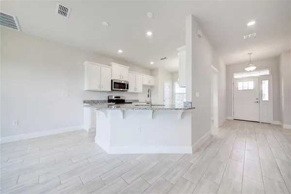 a view of an empty room with kitchen and window
