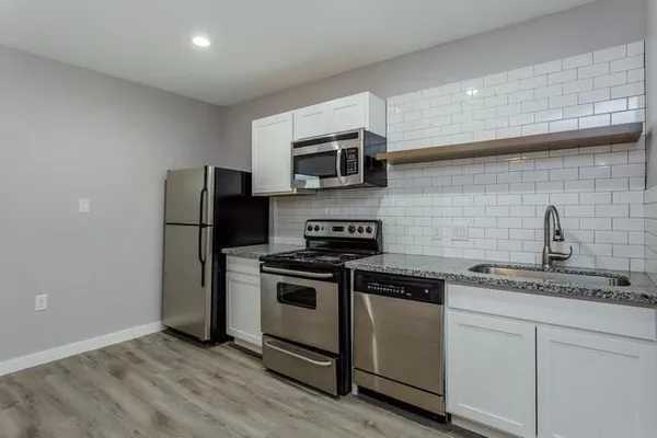 a kitchen with stainless steel appliances granite countertop white cabinets a refrigerator a stove a microwave oven and a sink with wooden floor