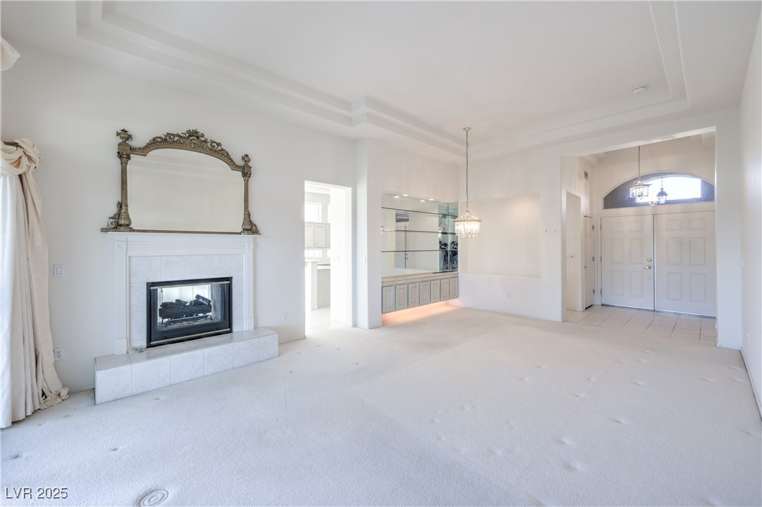 2404 Spring Water Drive Las Vegas, NV 89134 - Photo 18 of 27 Unfurnished living room featuring a tray ceiling, a chandelier, carpet floors, and a tiled fireplace