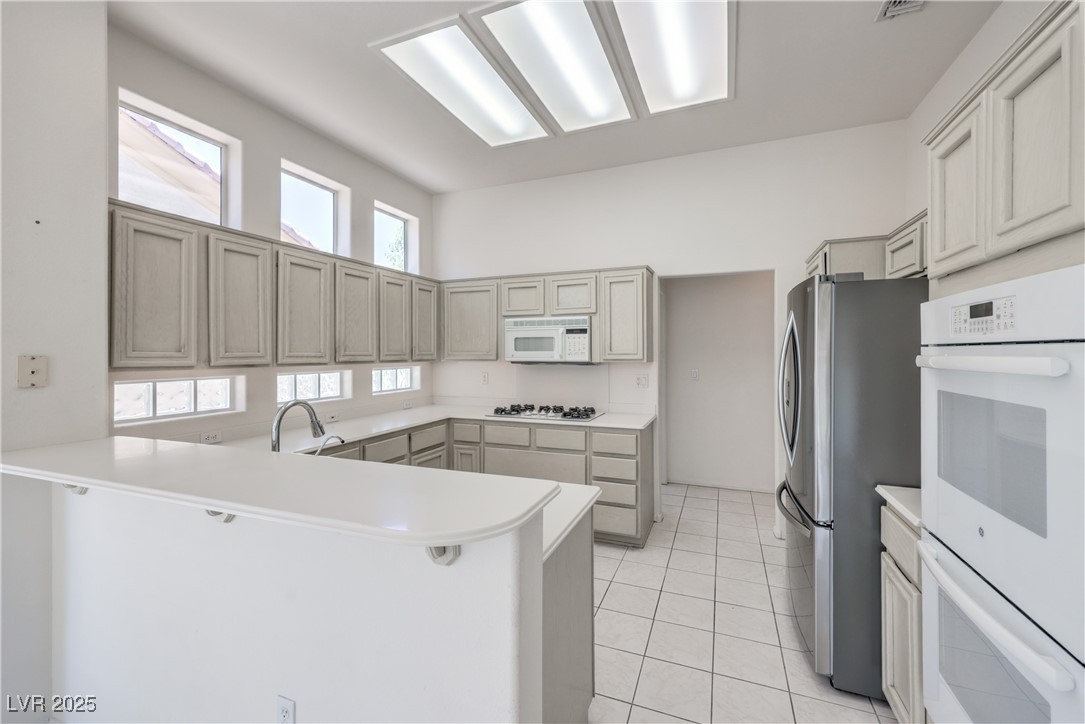 2404 Spring Water Drive Las Vegas, NV 89134 - Photo 4 of 27 Kitchen with white appliances, a peninsula, light countertops, and light tile patterned floors