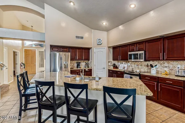 a kitchen with stainless steel appliances kitchen island granite countertop a dining table chairs sink and cabinets