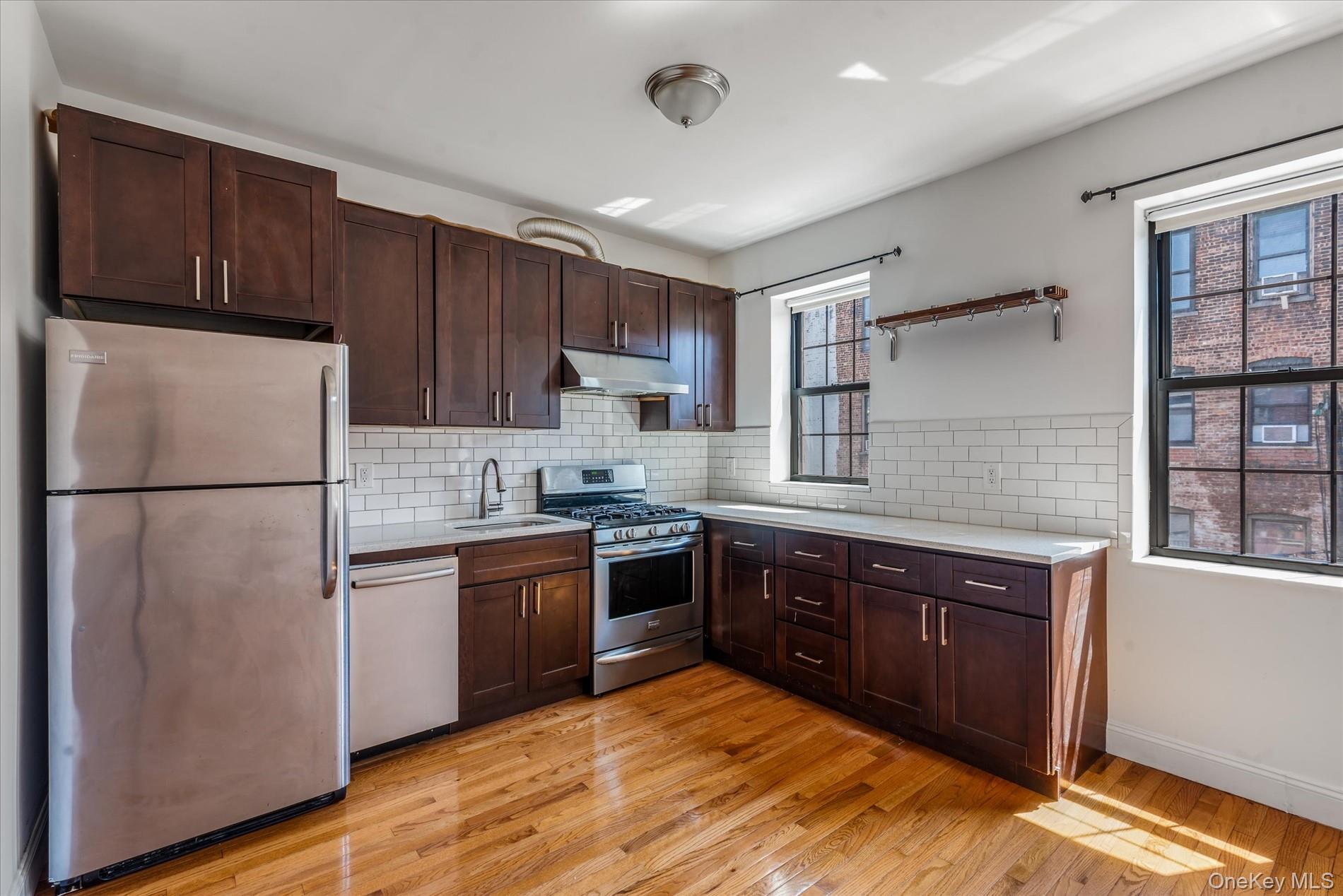 26-19 14th Place Queens, NY 11102 - Photo 22 of 33 Kitchen with appliances with stainless steel finishes, light countertops, dark brown cabinetry, and light wood finished floors