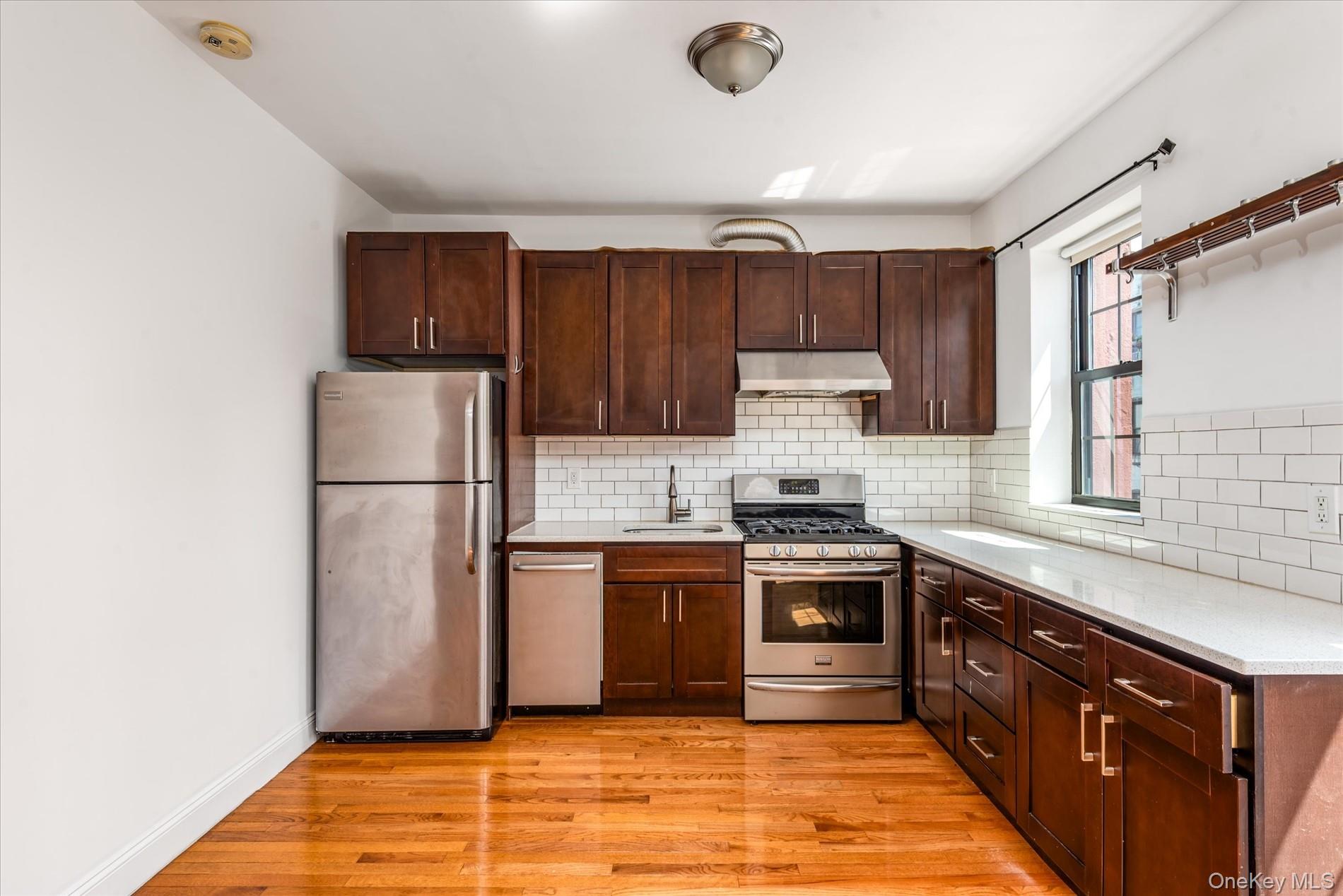 26-19 14th Place Queens, NY 11102 - Photo 23 of 33 Kitchen featuring stainless steel appliances, light wood-style flooring, light countertops, under cabinet range hood, and dark brown cabinets