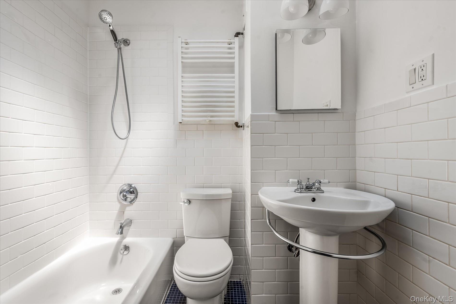 26-19 14th Place Queens, NY 11102 - Photo 30 of 33 Full bathroom featuring radiator, tile walls, bathing tub / shower combination, a towel warmer, and a wainscoted wall