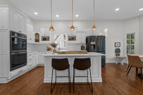 a kitchen with stainless steel appliances granite countertop a stove a sink a microwave a refrigerator and white cabinets with wooden floor