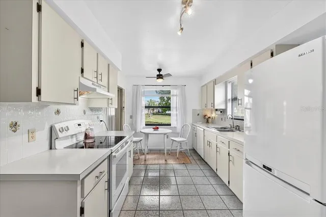 a large white kitchen with stainless steel appliances a stove a sink a refrigerator and cabinets