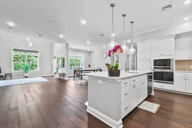 a kitchen that has a lot of white cabinets and couches with wooden floor