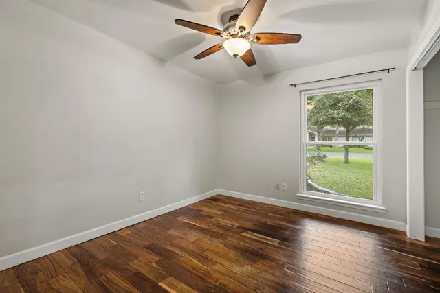an empty room with wooden floor fan and windows