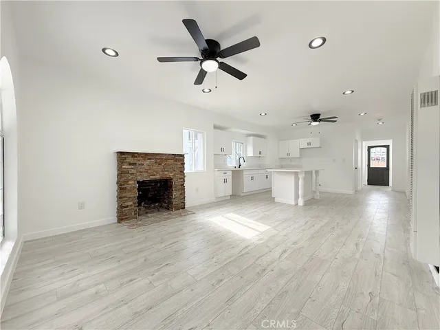 a view of a livingroom with a fireplace a ceiling fan and kitchen view