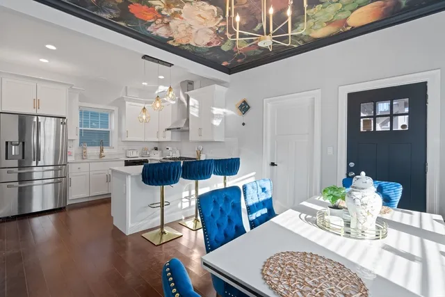 a kitchen with stainless steel appliances kitchen island granite countertop a dining table chairs and a refrigerator