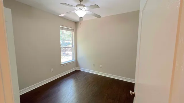 an empty room with wooden floor chandelier fan and windows