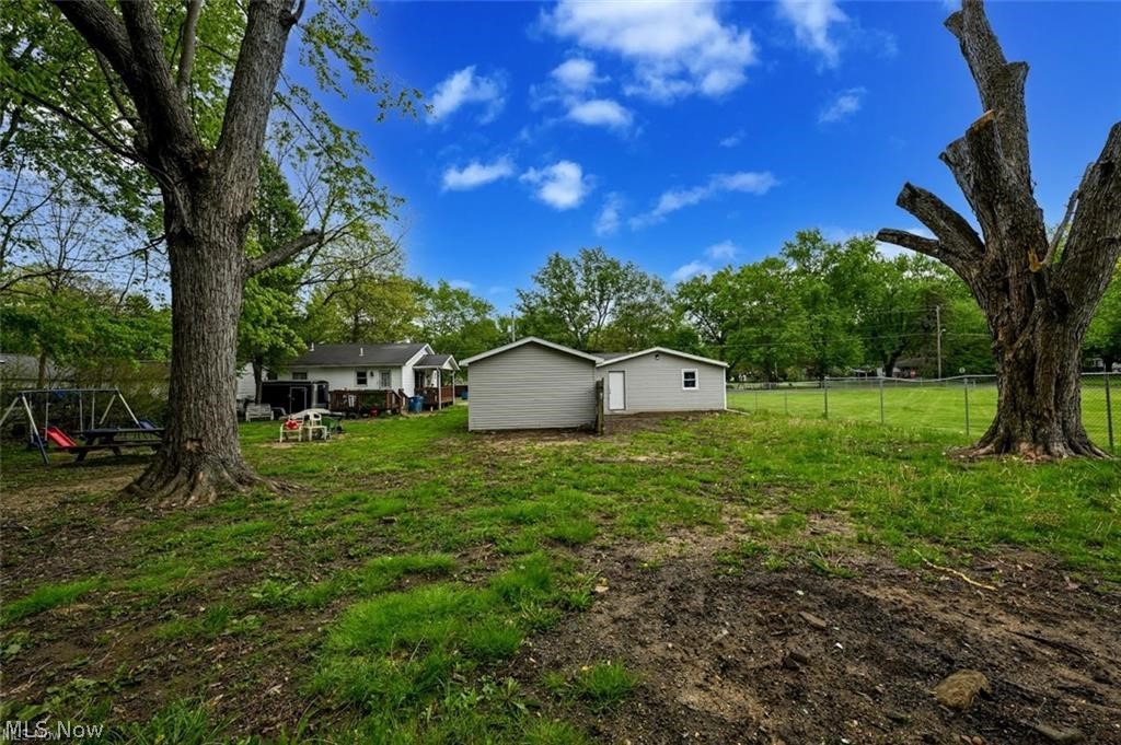 916 Abington Road Akron, OH 44312 - Photo 7 of 24 Expansive green space featuring two storage sheds, mature trees, and a chain-link fence