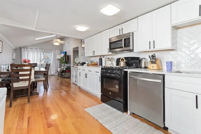 a kitchen with stainless steel appliances granite countertop a refrigerator a stove top oven a sink dishwasher and white cabinets with wooden floor