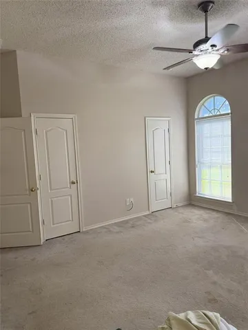 an empty room with chandelier fan and windows