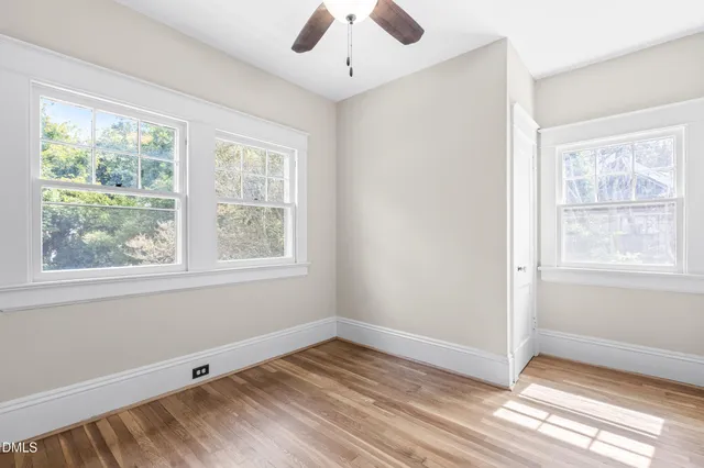 a big room with wooden floor a chandelier fan and windows